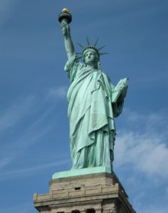 a statue of a woman holding a book and a torch with Statue of Liberty in the background