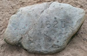 a large rock with numbers carved into it with Plymouth Rock in the background