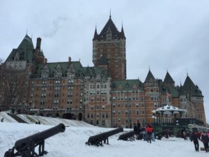 a large brick building with a large building and cannons in the snow with Château Frontenac in the background