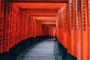 a walkway with red pillars with Fushimi Inari-taisha in the background