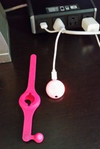 a pink wrist watch with a hole in the center next to a white cord