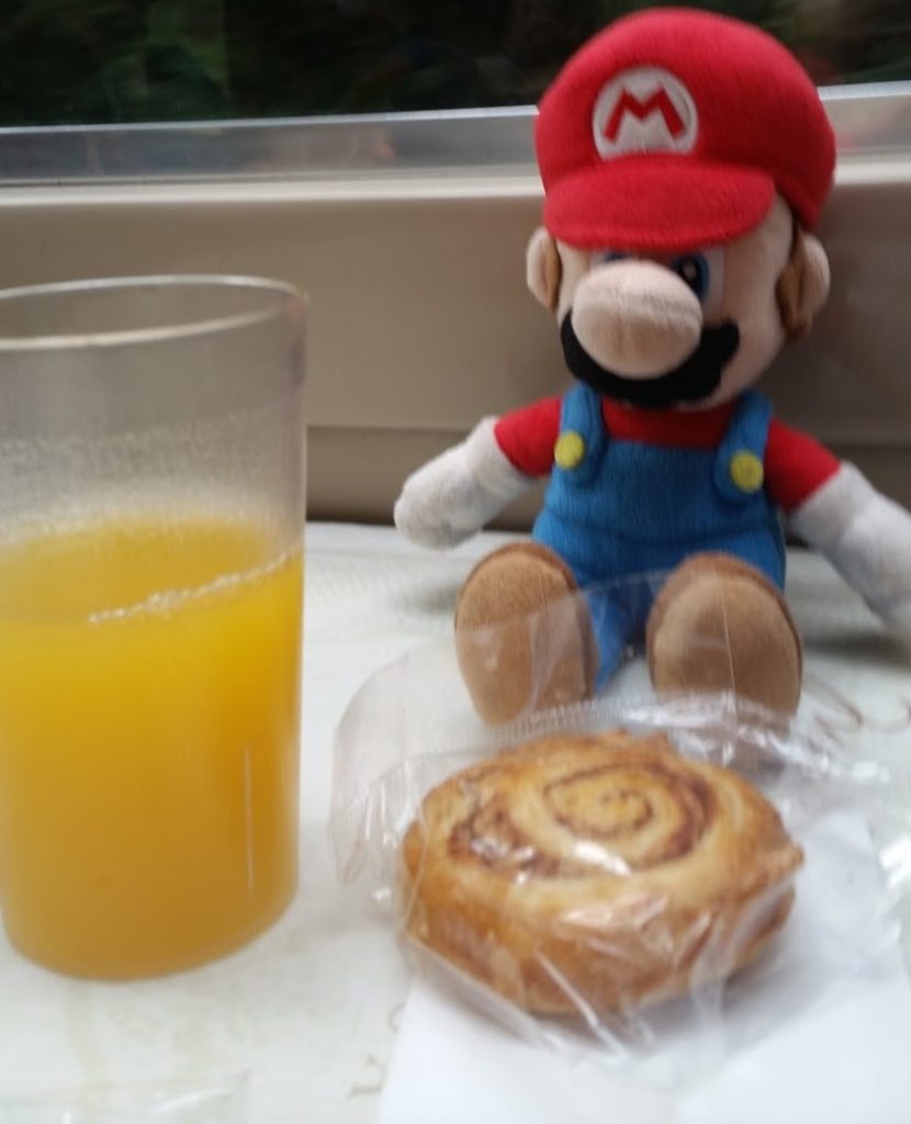 a stuffed toy and a cinnamon roll next to a glass of juice