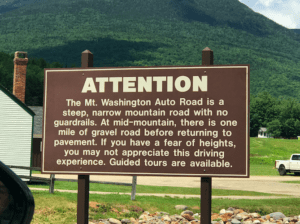 a brown sign with white text and a mountain in the background