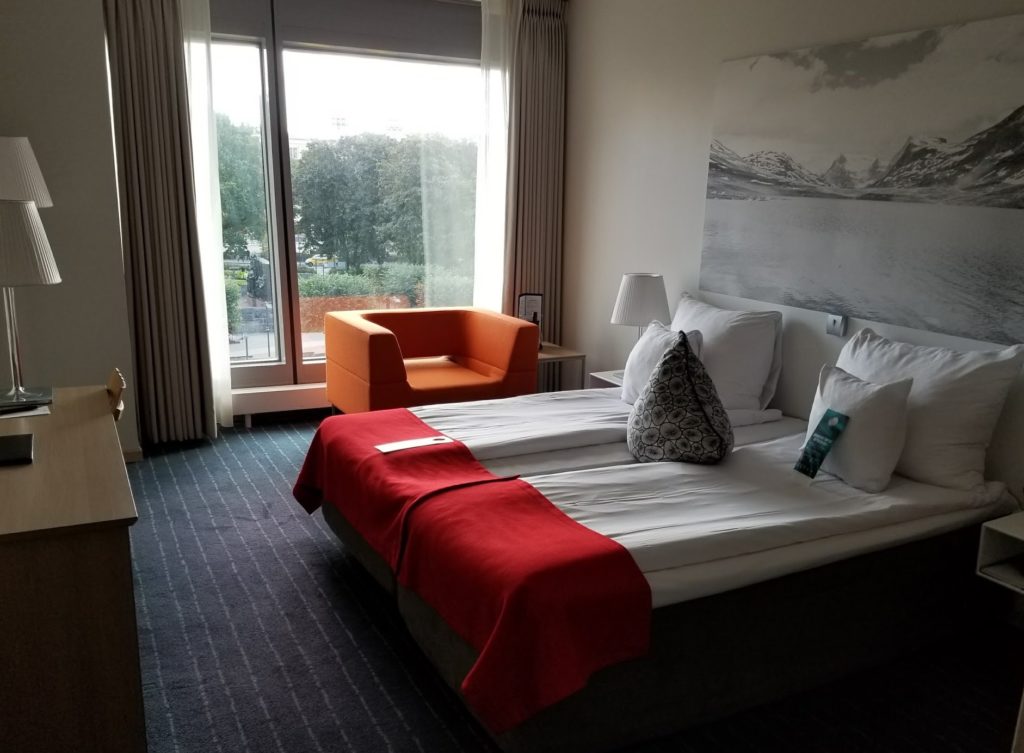 a bed with a red blanket and a chair in a hotel room