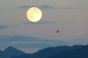 a helicopter flying in the sky with the moon in the background