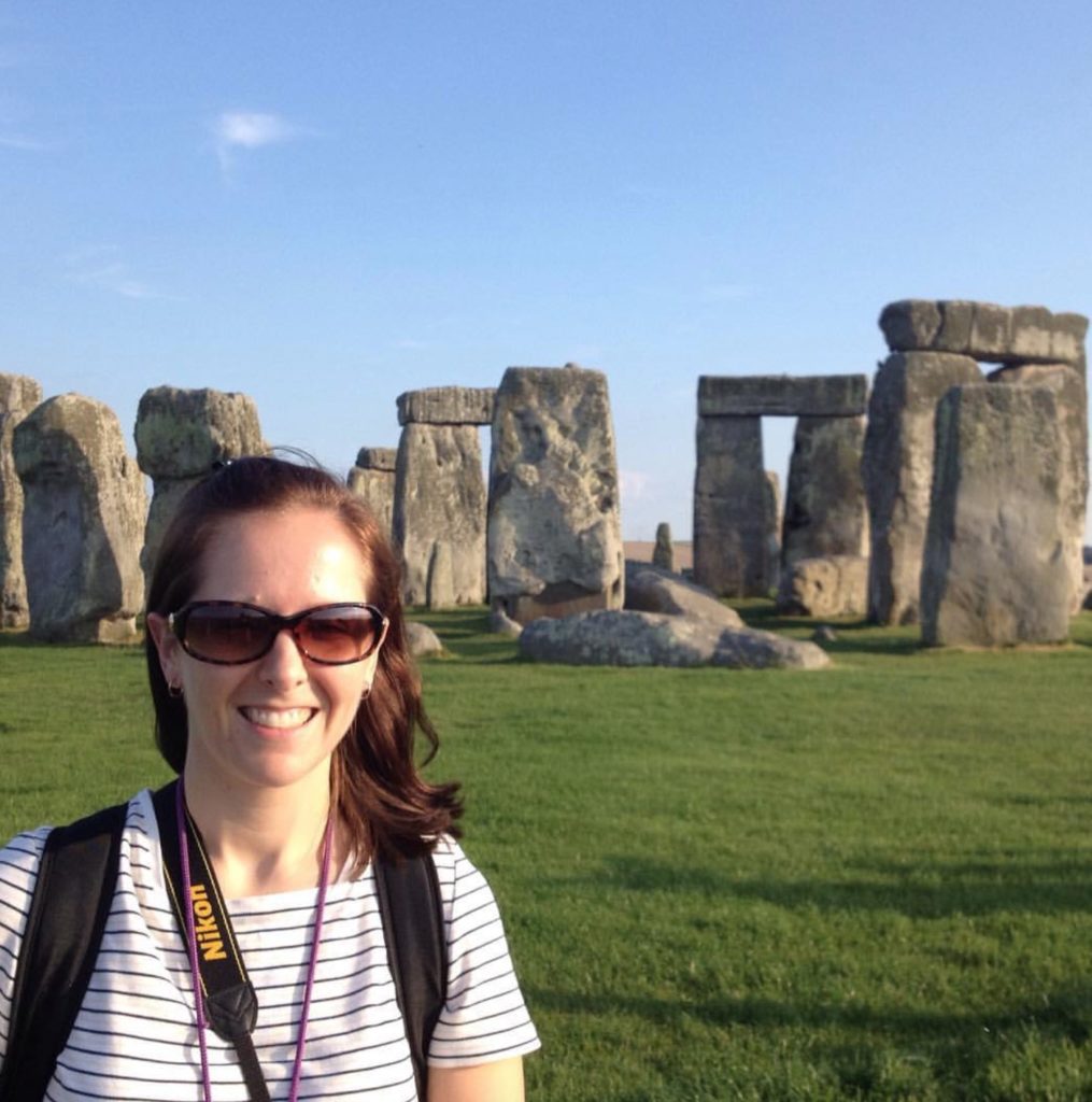 a woman standing in front of a stone monument with Stonehenge in the background