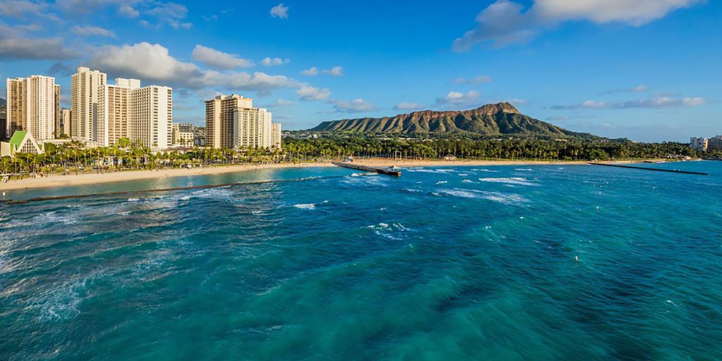 a body of water with a beach and Diamond Head in the background
