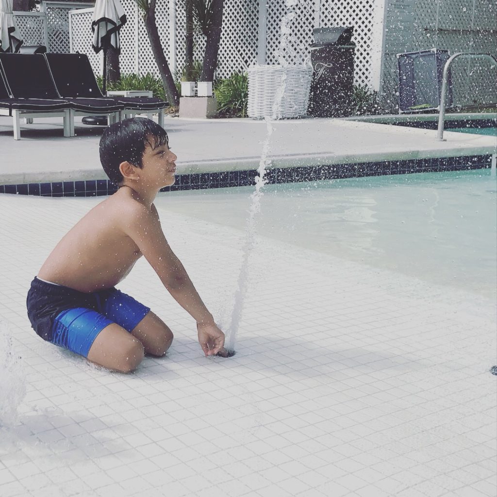 a boy sitting in a pool with water spraying