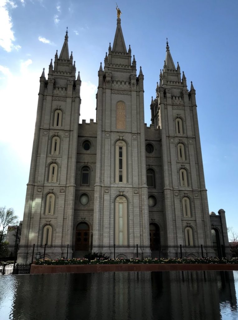 a large stone building with towers with Salt Lake Temple in the background