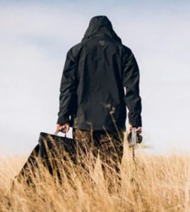 a person in a black coat holding a bag in a field