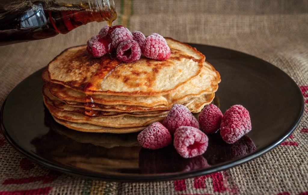 a stack of pancakes with raspberries and syrup on a black plate