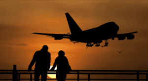 silhouette of people looking at an airplane flying over a railing