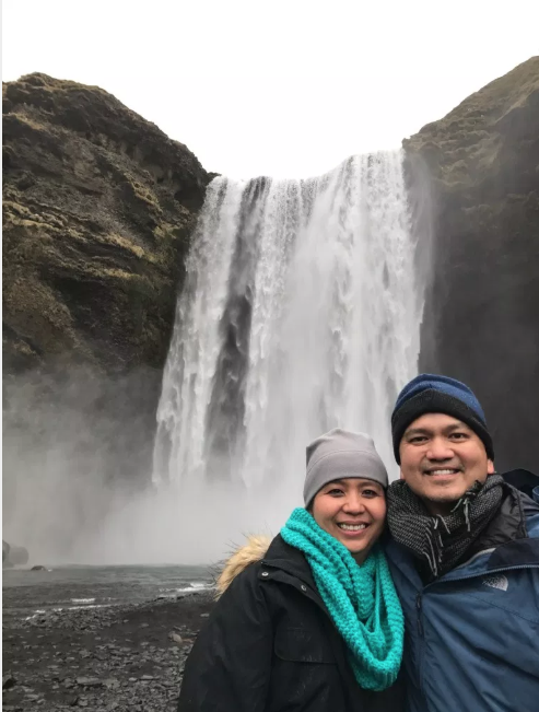 a man and woman standing in front of a waterfall