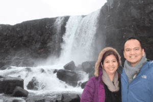a man and woman standing in front of a waterfall