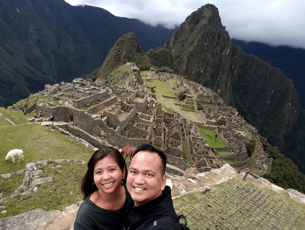 a man and woman taking a selfie with a stone structure in the background