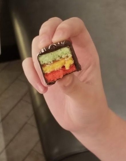 a hand holding a piece of chocolate with a rainbow colored cake