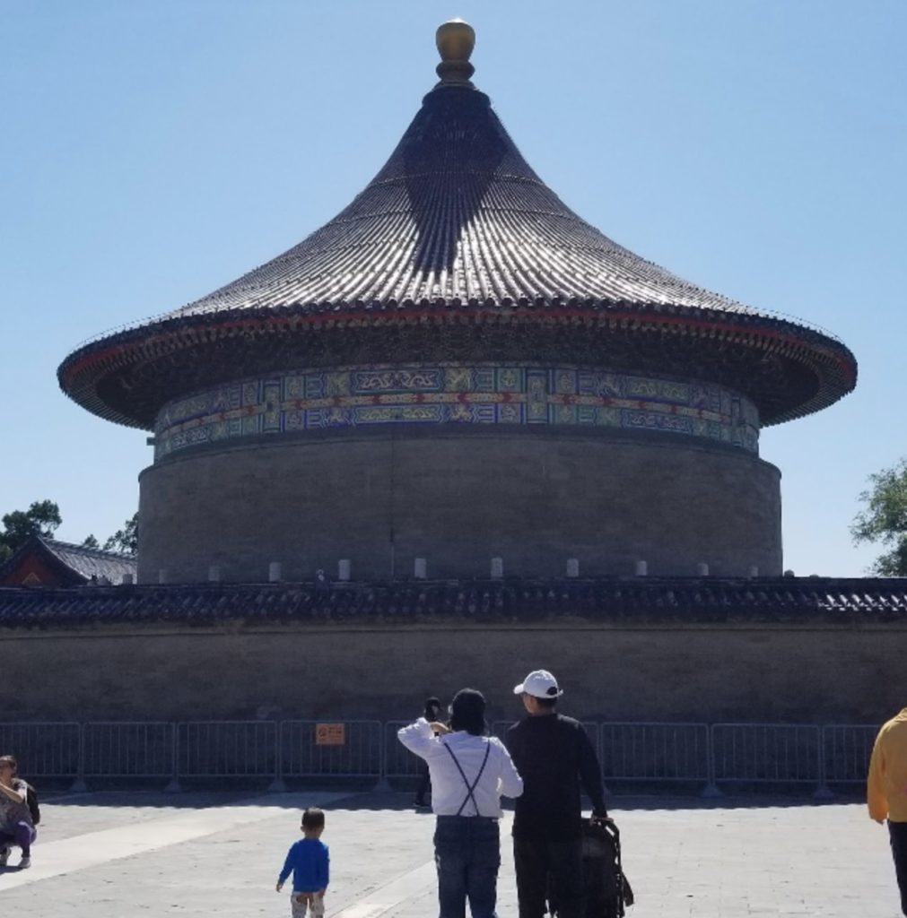 a group of people standing in front of a round building with Temple of Heaven in the background