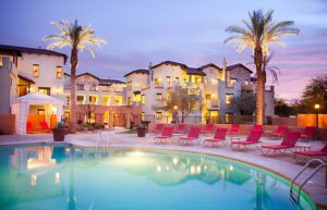 a pool with lounge chairs and palm trees in front of buildings