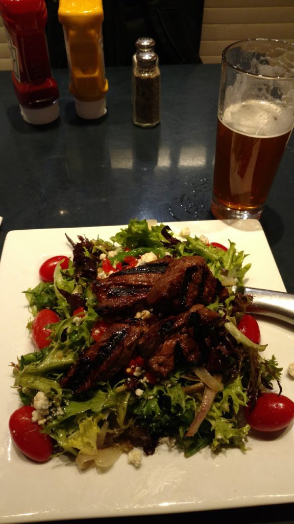 a plate of salad with meat and a glass of beer