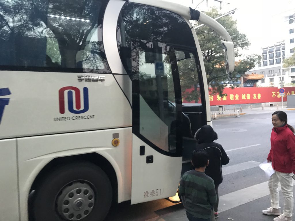 a white bus with a couple of kids standing on the side of the road