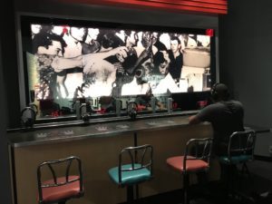 a man sitting at a bar with a large screen