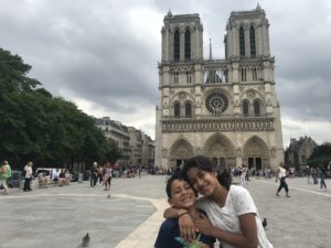 two girls posing for a picture in front of a large building with Notre Dame de Paris in the background