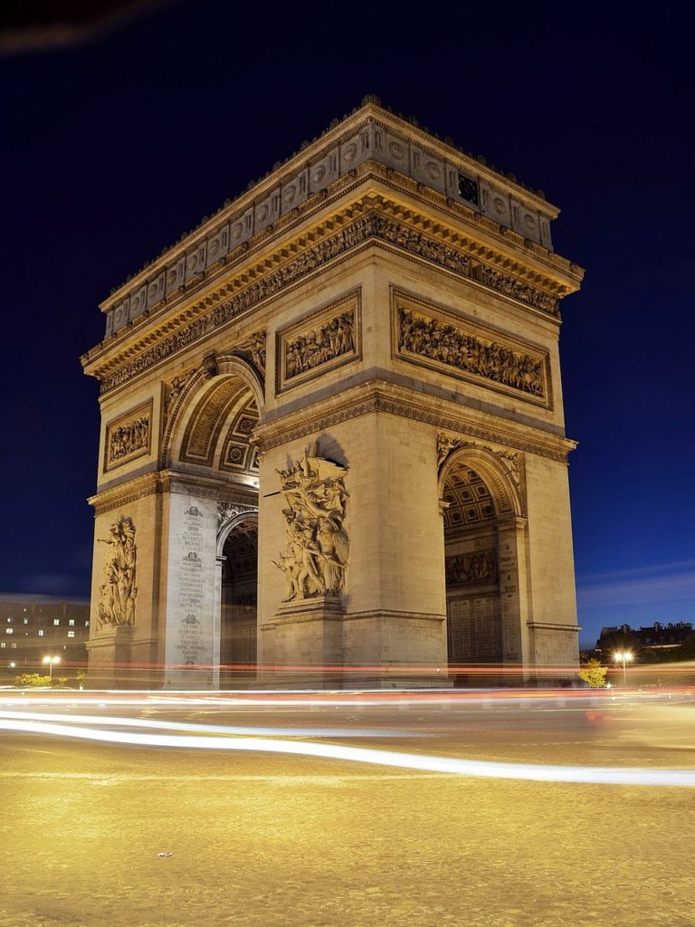 a large stone arch with carvings on it with Arc de Triomphe in the background