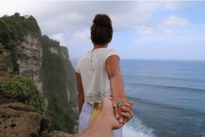 a woman holding a hand of a man on a cliff overlooking the ocean