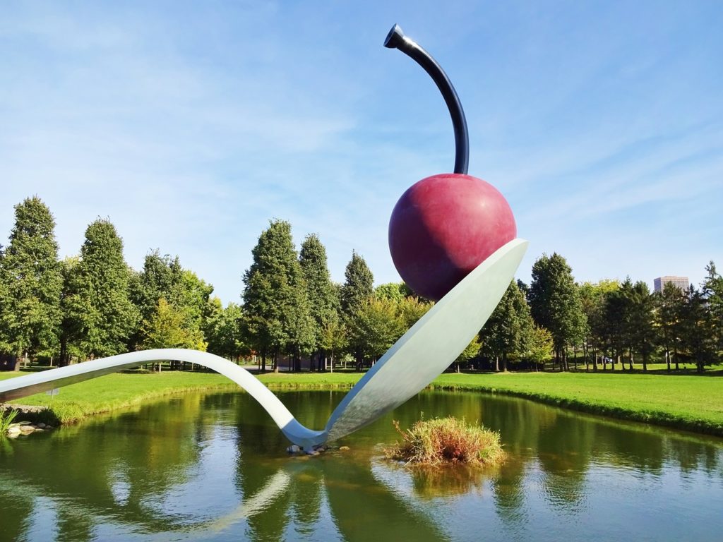 a spoon and a cherry on a spoon with Minneapolis Sculpture Garden in the background