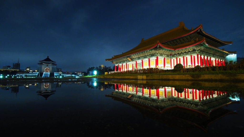 a building with red pillars and lights reflecting in water