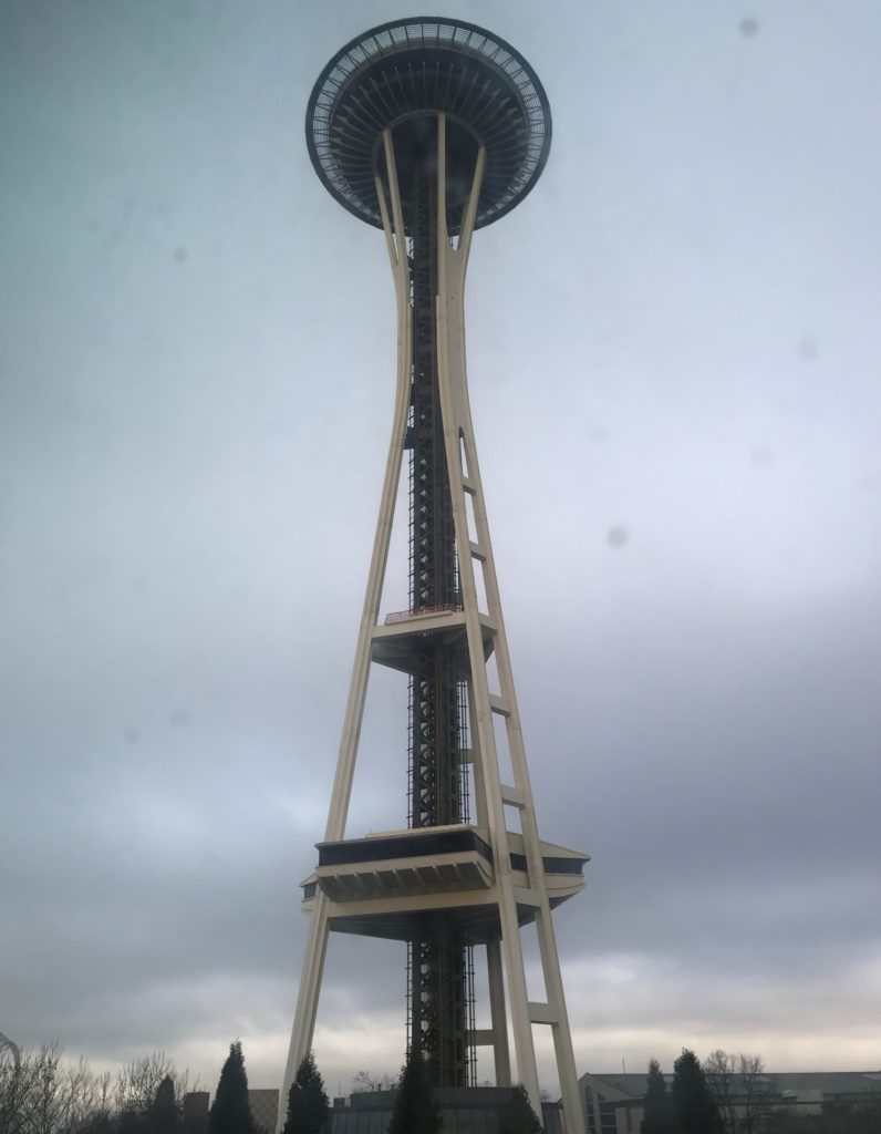 a tall tower with a round top with Space Needle in the background