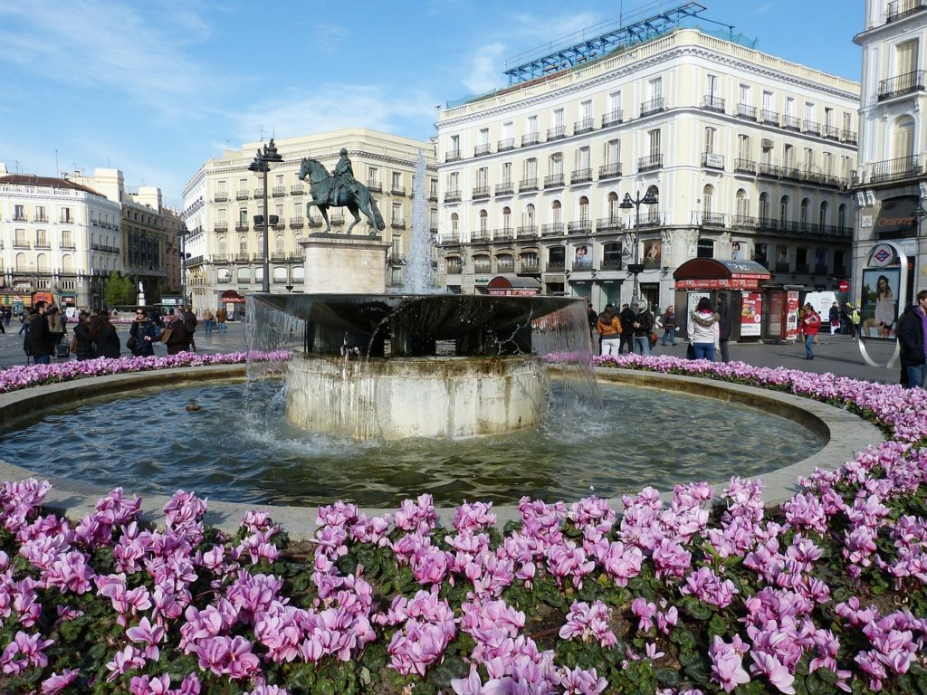 a fountain with a statue of a horse and flowers in front of a building