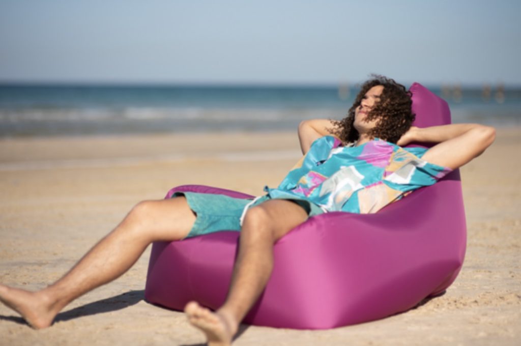 a person lying on a purple bean bag on the beach