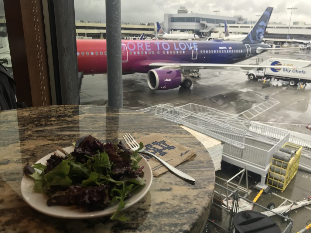 a plate of salad on a table with a plane in the background