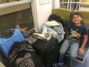 a boy and girl sitting on a train seat with luggage