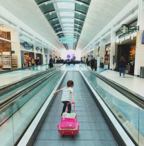 a child pushing a pink suitcase in a mall