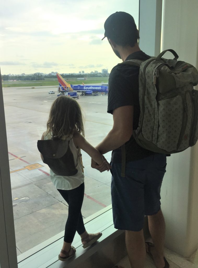 a man and child holding hands looking out a window at an airport