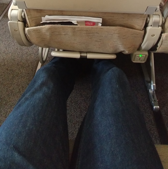 a person's legs in jeans and a tan pocket on a seat