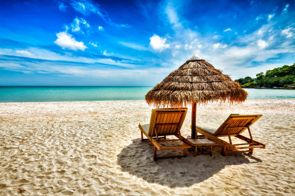 Two empty chairs sit under shade on a beach.