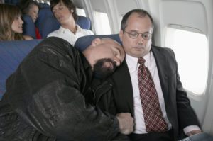 A man has laid his head on another man on an airplane.