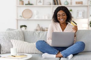 a woman sitting on a couch holding a credit card and using a laptop