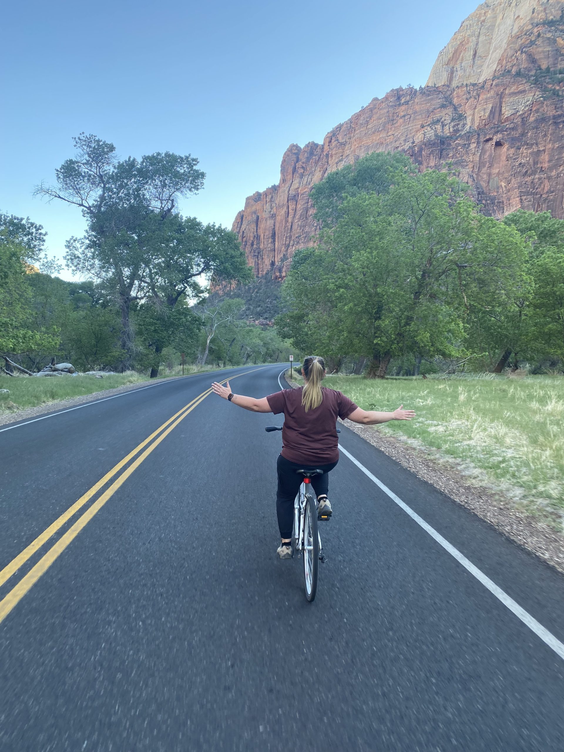 a woman riding a bicycle on a road with trees and mountains