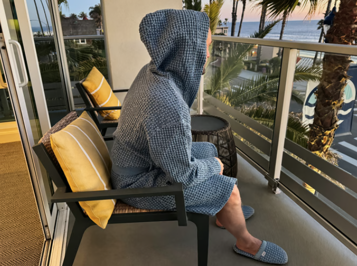 a person wearing a robe sitting on a chair looking out to the ocean