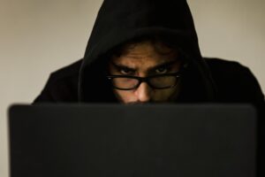 a man wearing glasses and a hood looking at a laptop