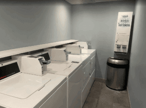 a laundry room with white washers and a trash can