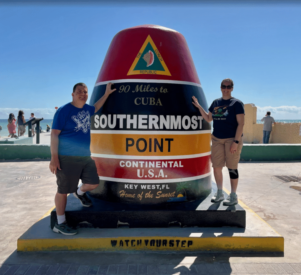 two men standing next to a large cone with Southernmost point buoy in the background